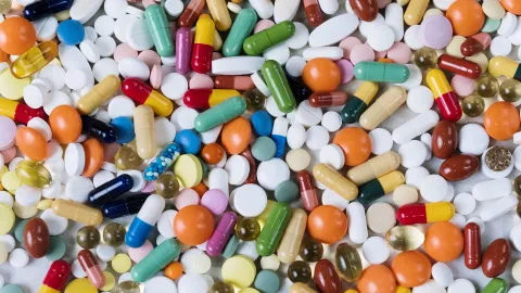 A colourful flat lay of assorted pills and capsules in red, yellow, orange, green, blue and white, densely packed together.